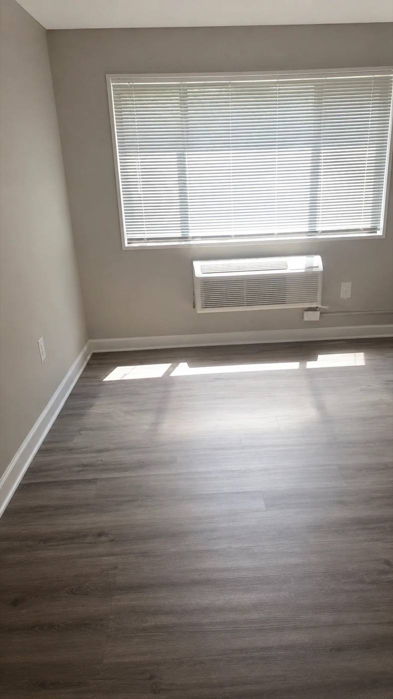 A renovated bedroom with plank flooring and a window unit